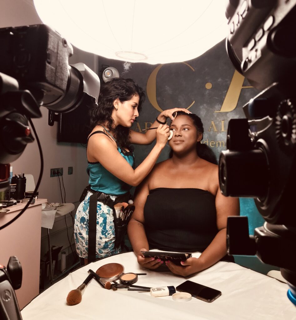 Maquilladora aplicando maquillaje profesional en modelo durante clase práctica en academia