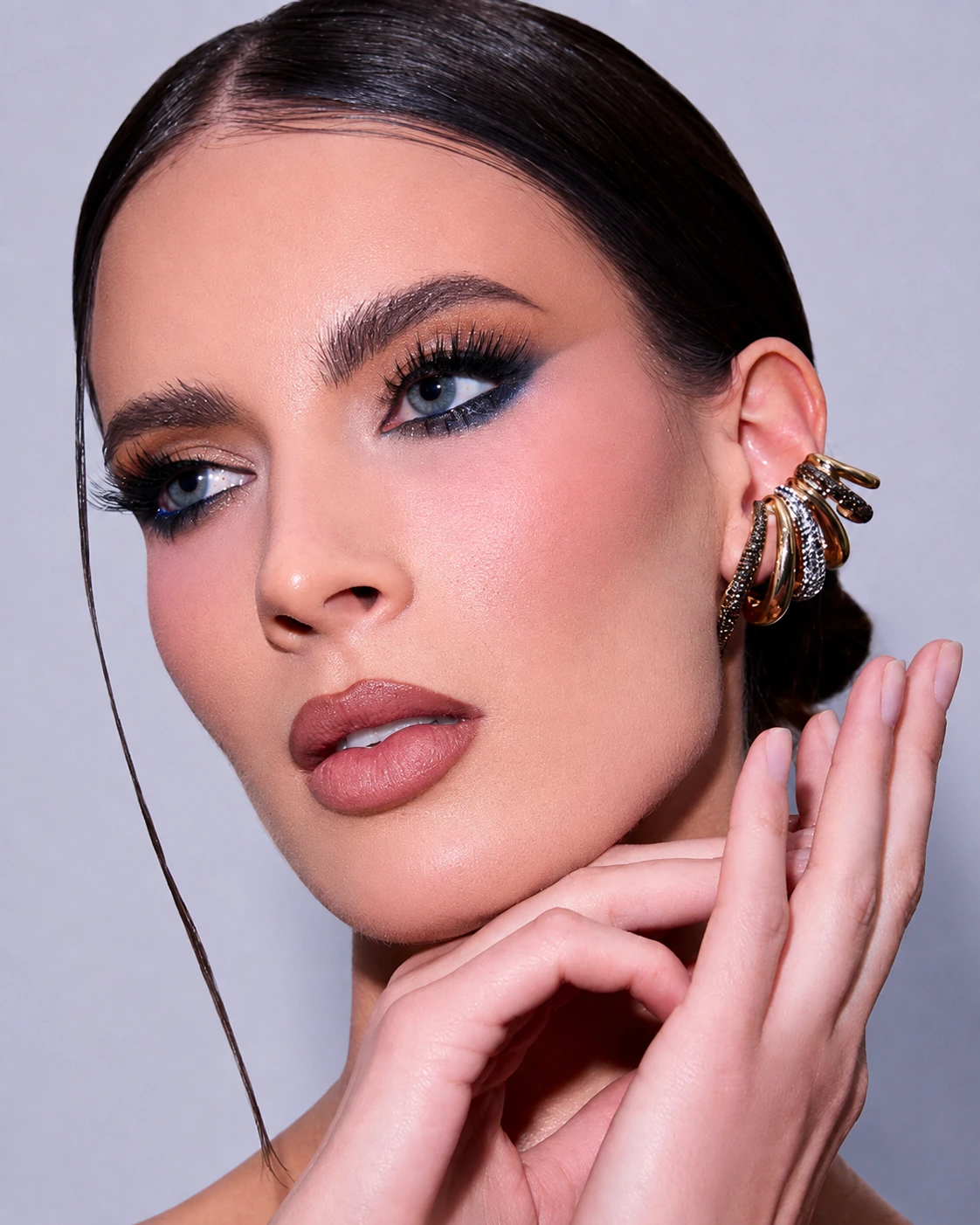 Modelo con maquillaje editorial azul ahumado, piel luminosa y joyería dorada
