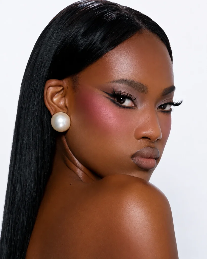 Modelo de piel oscura con maquillaje editorial, delineado alargado y rubor rosa