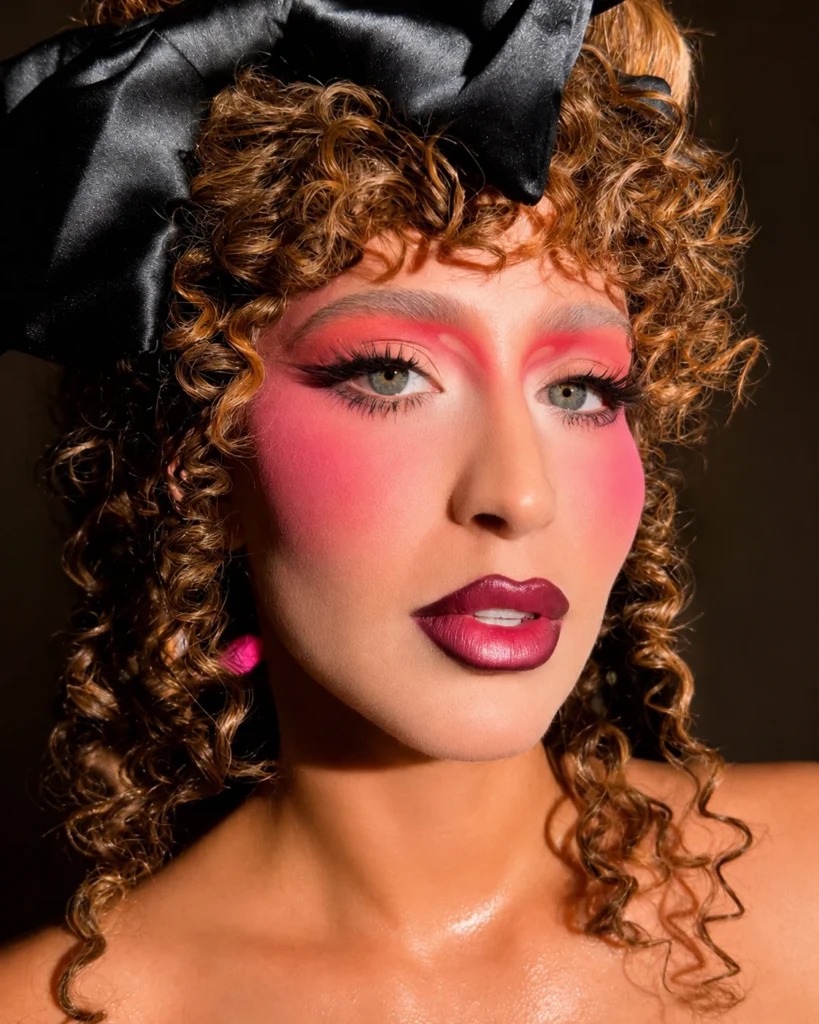 Modelo con maquillaje editorial rosa, labios color vino, rizos definidos y lazo negro