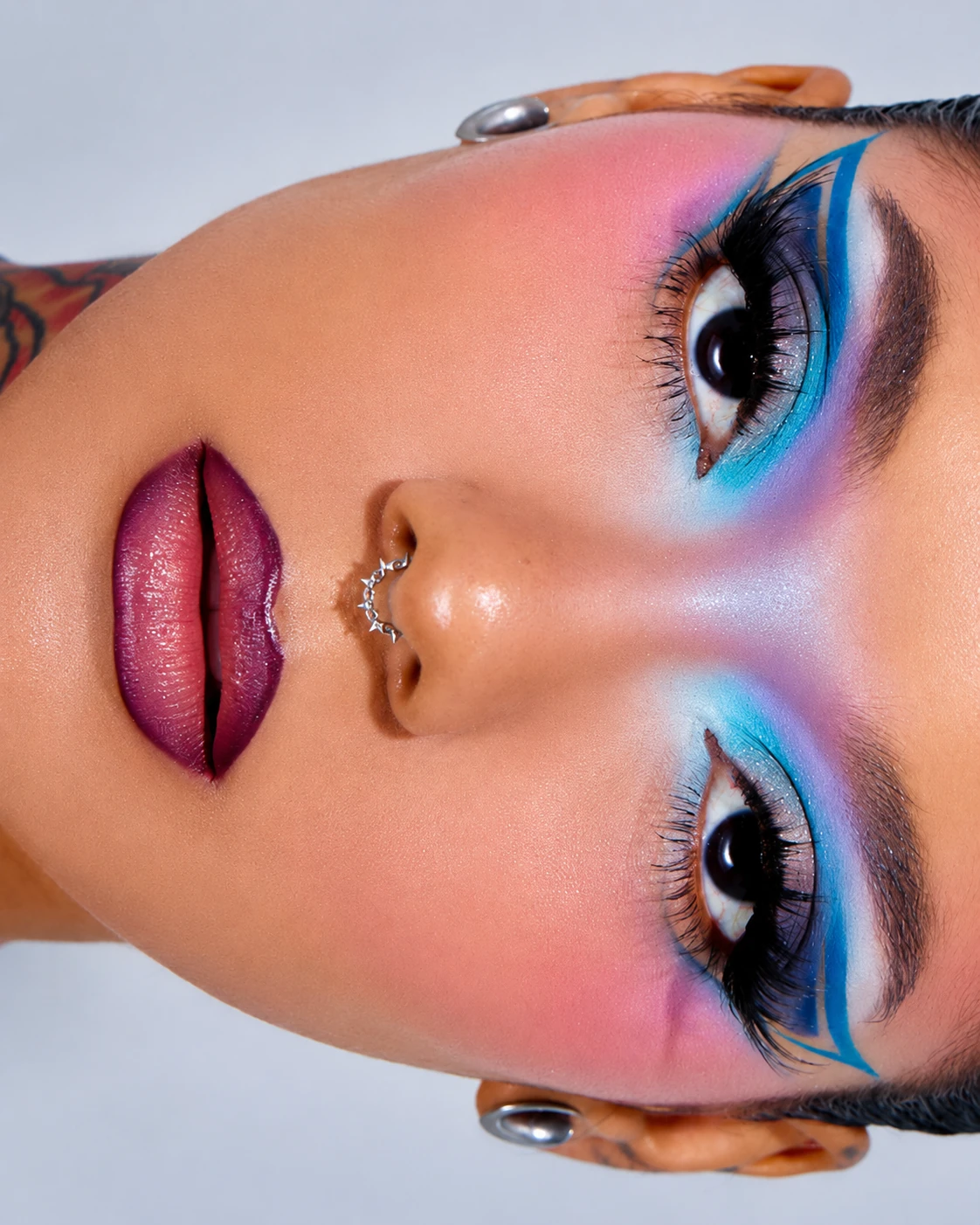 Primer plano de maquillaje futurista azul y rosa con delineado gráfico y labios morados.