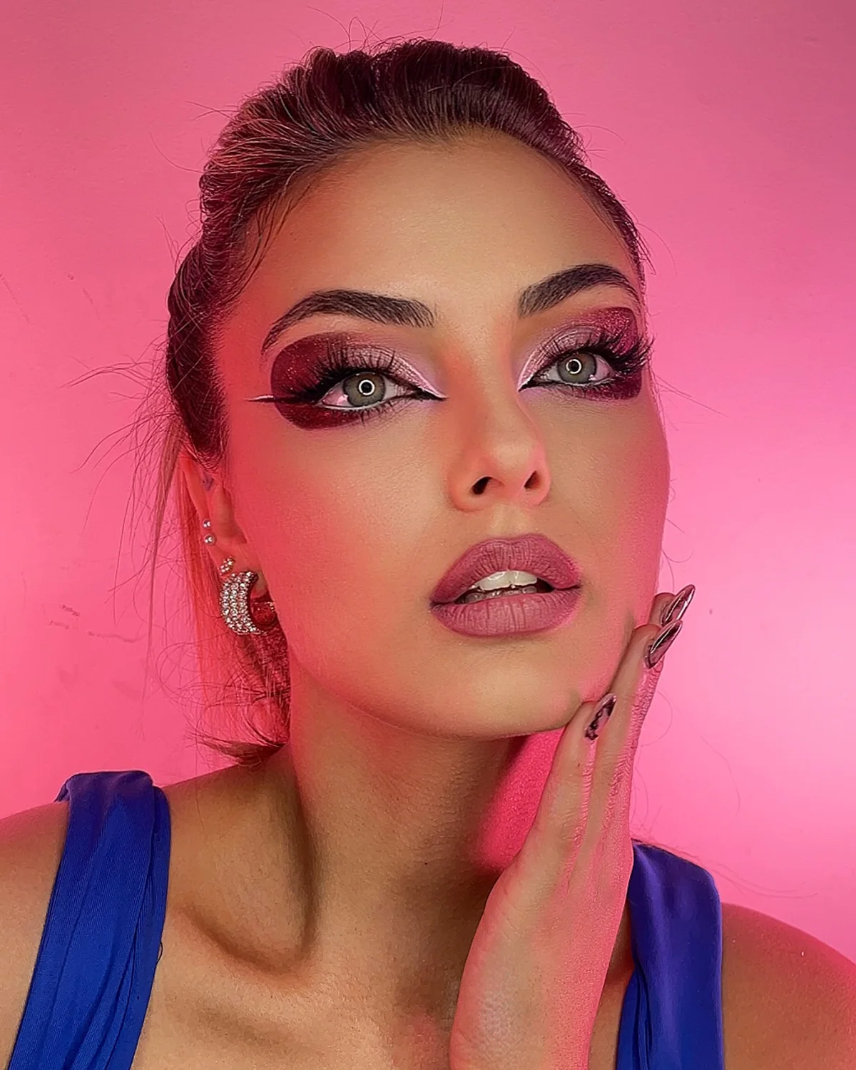 Maquillaje creativo en tonos rosa y violeta con delineado blanco sobre fondo fucsia