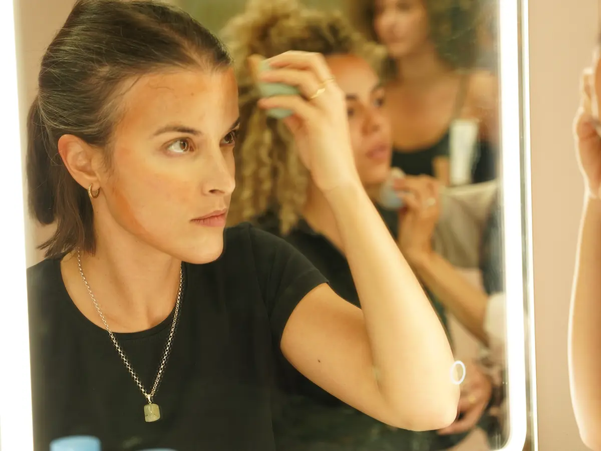 Organización y limpieza del kit de maquillaje Alumna practicando frente a un espejo con productos de maquillaje organizados en la mesa