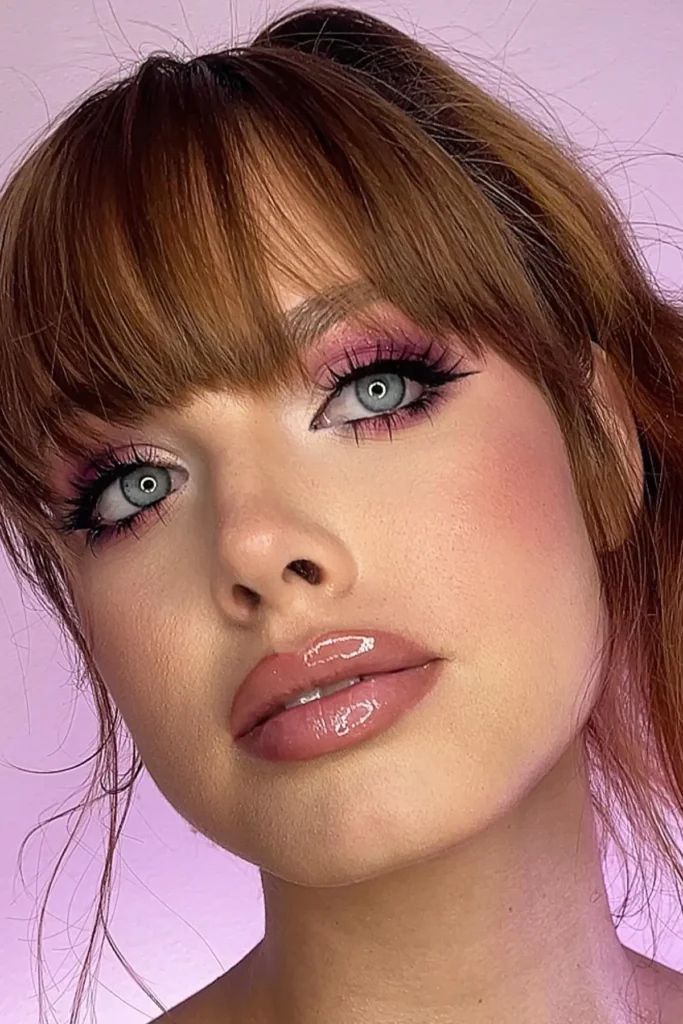 Primer plano de una mujer pelirroja con maquillaje de ojos rosado y piel luminosa